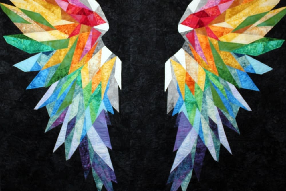 Rainbow colored wings quilted on a black background quilt. 