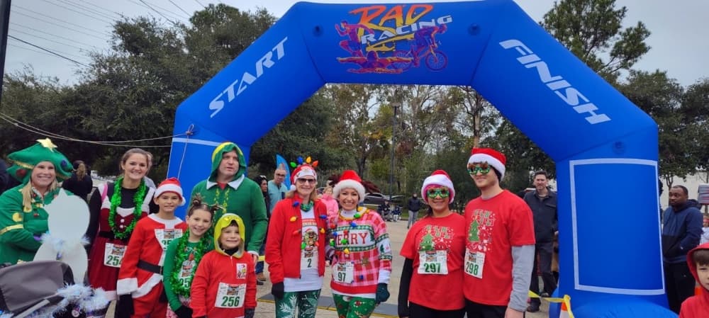 people in red shirts and santa hats under a race starting line arch