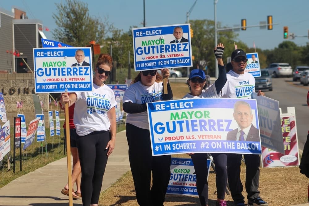 Shelby Dugie, Raquel E. Gutierrez and Raquel Gutierrez stand outside the Guadalupe County Annex building with 're-elect Mayor Gutierrez' signs on Election Day. (Amira Van Leeuwen/Community Impact)