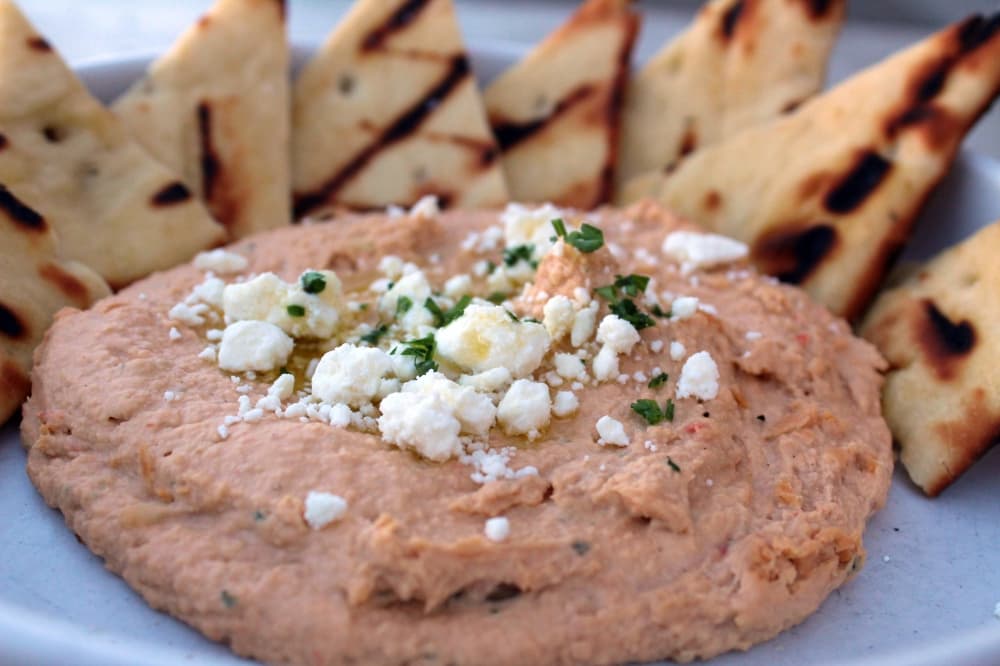 Hummus on a plate topped with cheese with a side of pita bread. 