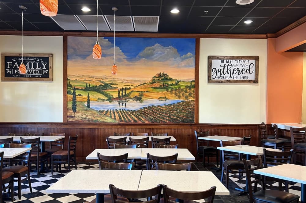 Interior of a restaurant featuring a countryside mural. 