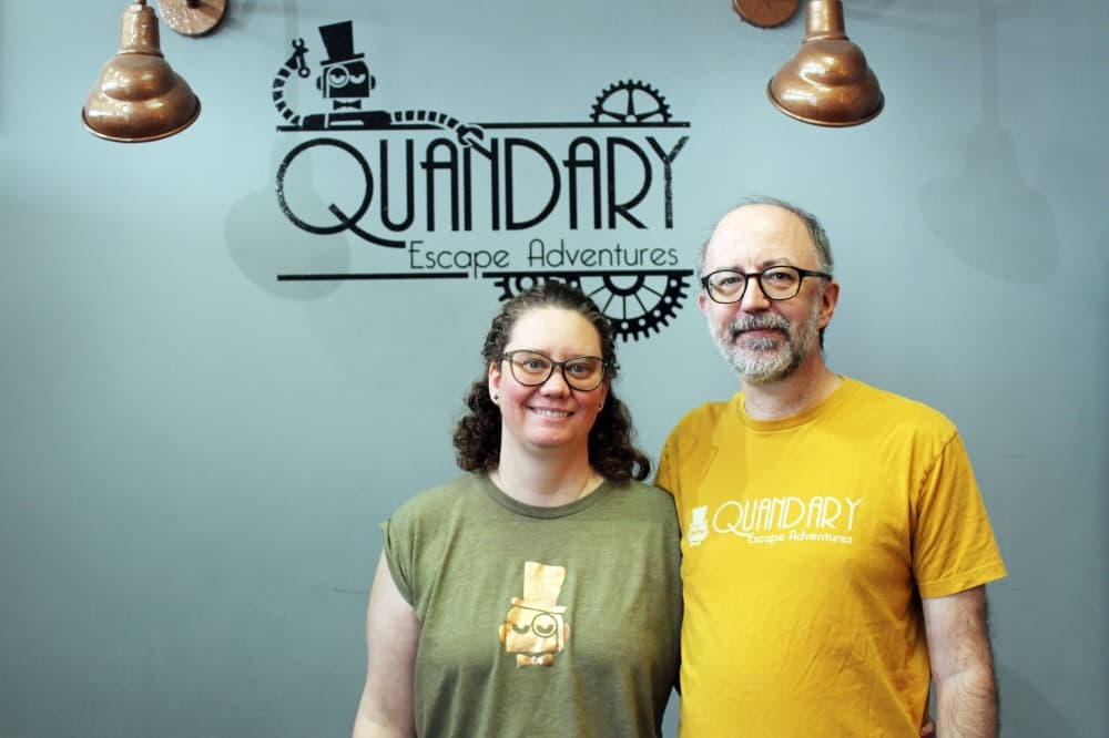Female and male standing beside each other in front of a wall featuring The Quandary signage. 