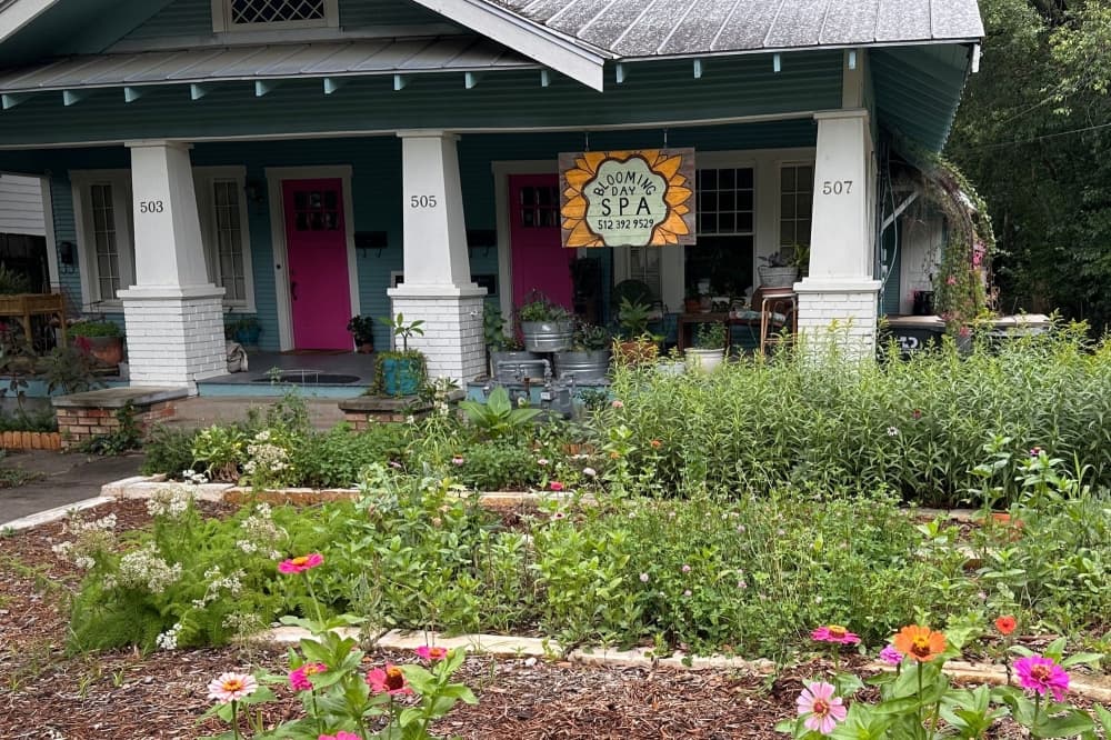 The grey and white exterior is shown with flowers and other greenery in the front yard.