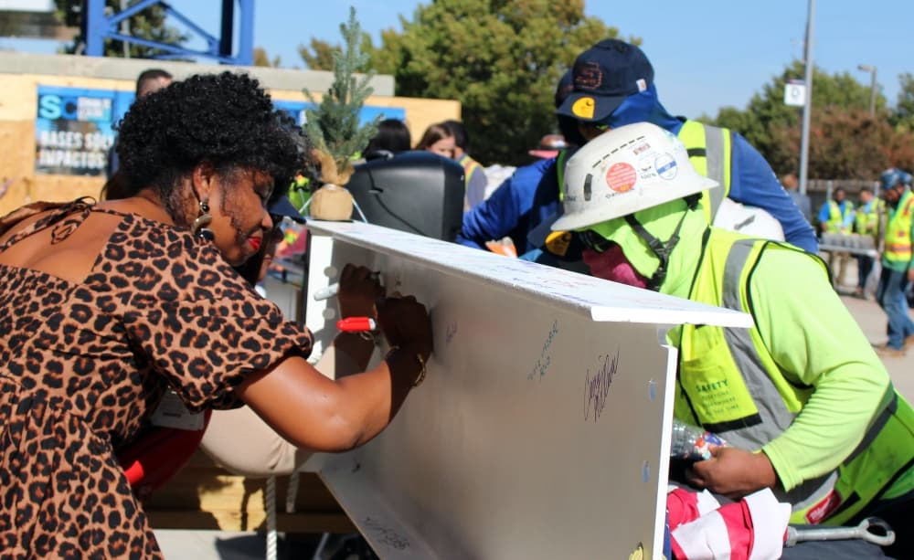 Female and males signing a construction beam. 