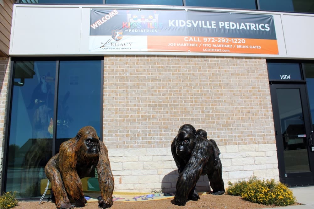 Exterior of a building featuring Kidsville Pediatrics temporary banner and statues of guerillas. 