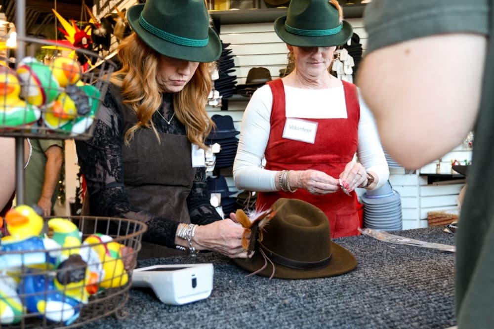 A vendor puts finishing touches on a traditional fedora for a customer at Wurstfest 2025. (Ethan Thomas/Community Impact)
