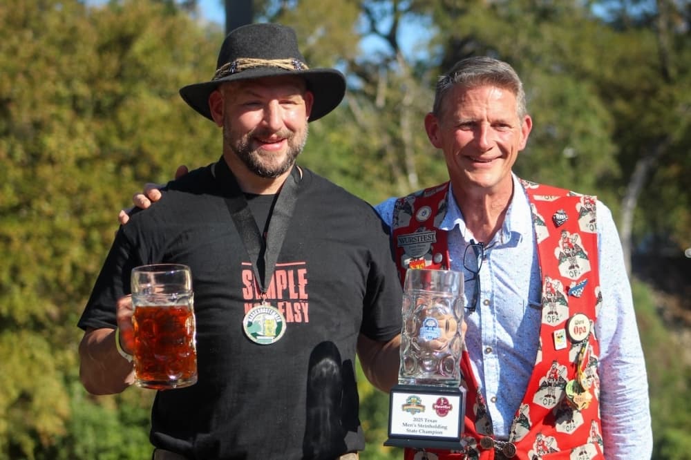 Cody Bane holds a stein of beer next to Jason Hurta, Wurstfest director and security chair, after winning the 2025 Texas Steinholding State Championship Finals at Wurstfest on Nov. 16. Bane held his stein for 12 minutes and 7 seconds. (Amira Van Leeuwen/Community Impact)