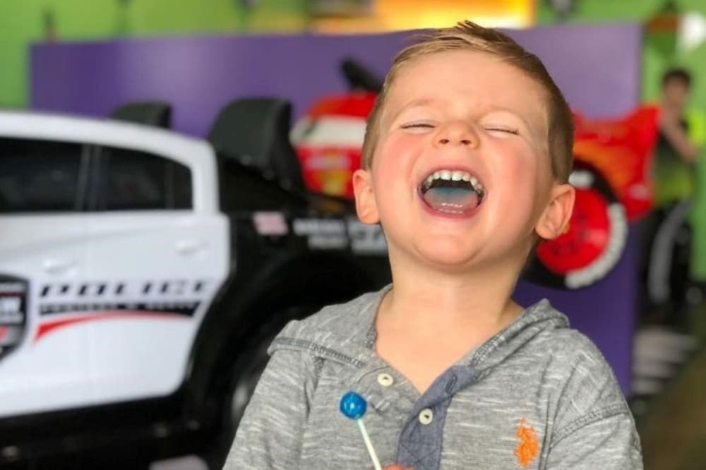 a boy laughs with a blue lollipop in his hand