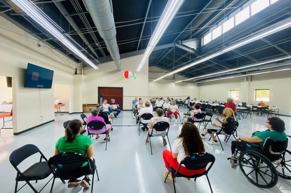A group of seniors in Cibolo, Texas are seen playing a game of indoor volleyball while sitting in chairs.