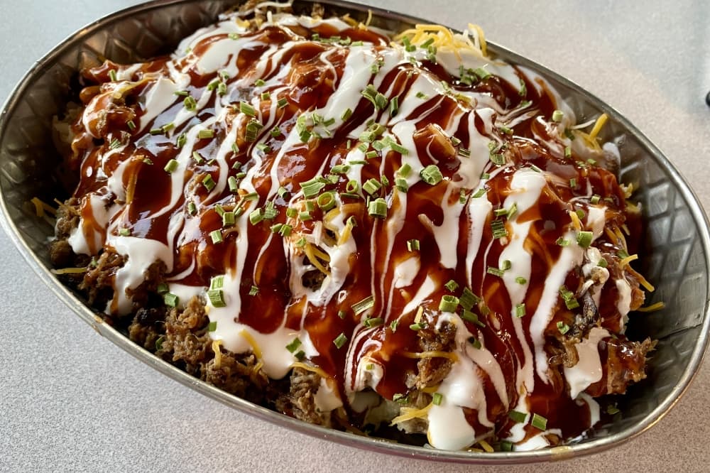 Menu items include the Alamo, which features smoked brisket on a spud with barbecue baked beans, sour cream, cheese, chives and barbecue sauce (Jr $18.25, Mega $24). (Katlynn Fox/Community Impact) 