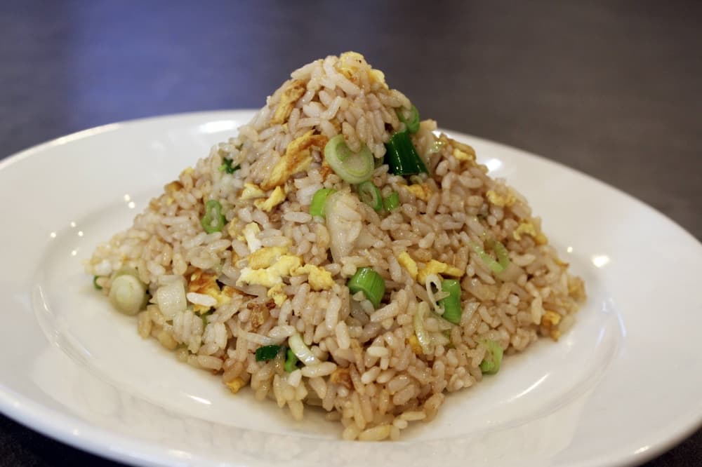 Fried rice featuring eggs and vegetables shaped into a dimensional pyramid on a white plate. 