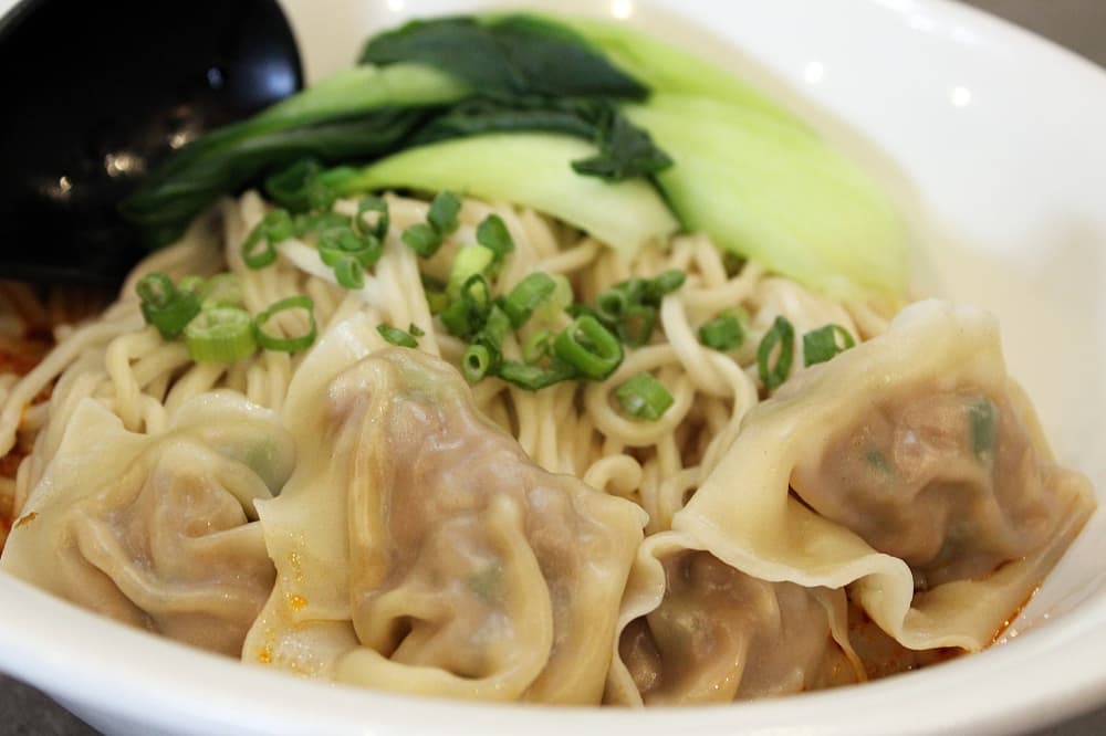 Noodles and steamed dumplings in a white bowl. 