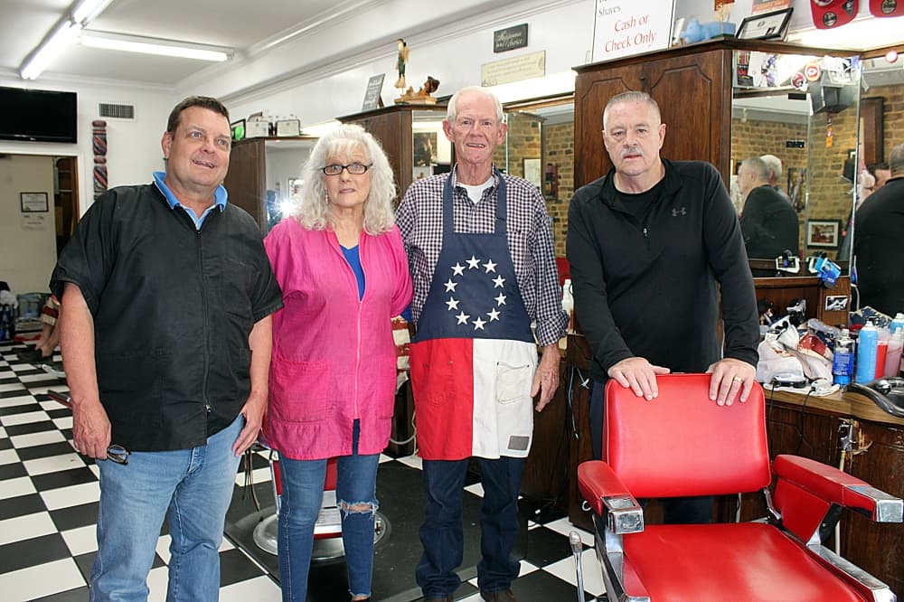 Three males and one female standing in a barber shop. 