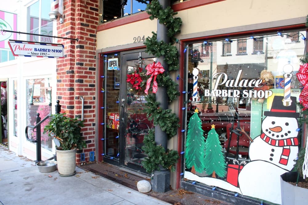 Exterior of a store featuring Palace Barber Shop signage and Christmas murals on the window. 
