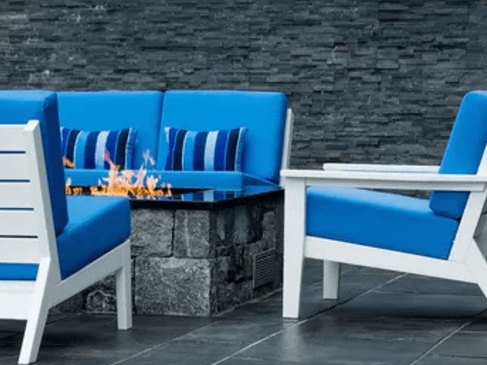 A modern outdoor seating area featuring bright blue cushions and a built-in stone fire pit.