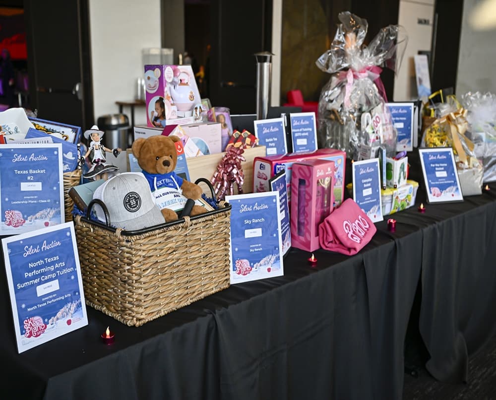 Silent auction baskets and prize packages line the display table at SKI Plano, offering guests a variety of unique items to bid on.