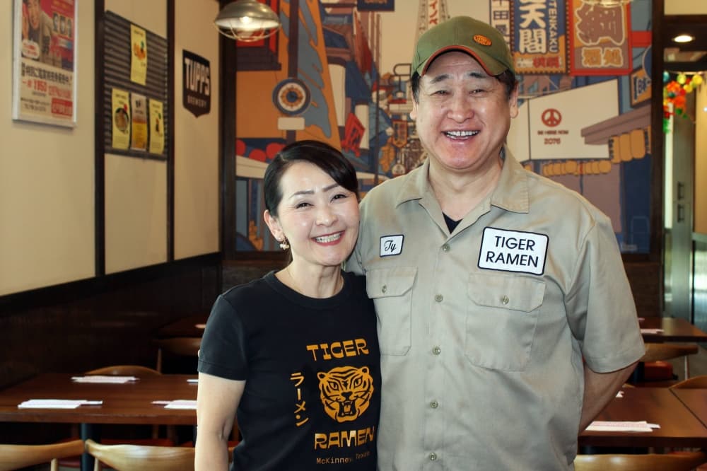 Female and male standing next to each other wearing Tiger Ramen branded shirts in a restaurant. 