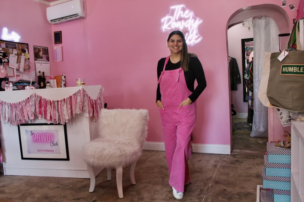 a woman dressed in pink overalls stands in front of a pink wall