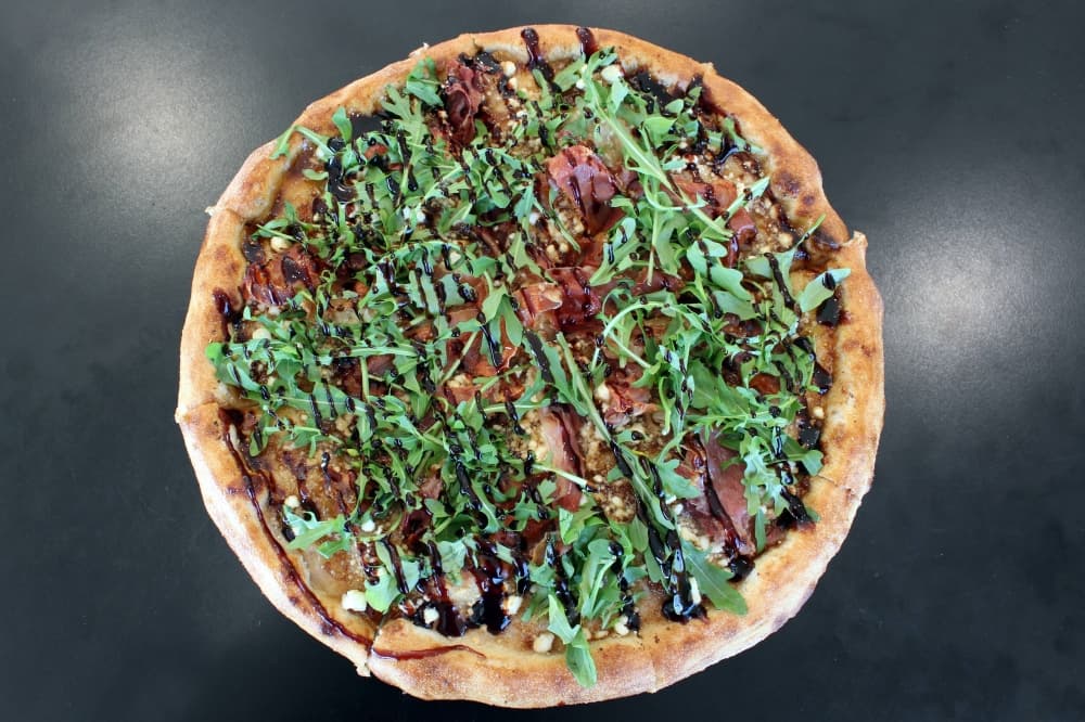 Overhead view of a pizza featuring arugula, meat and balsamic drizzle. 