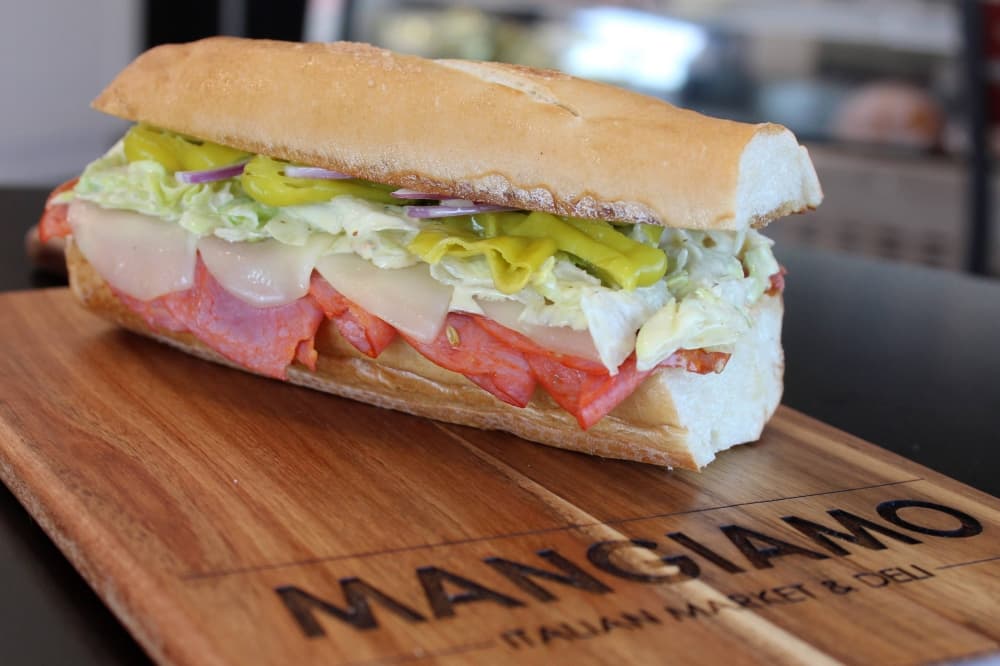 Sub sandwich on a wood board featuring Mangiamo branding. 
