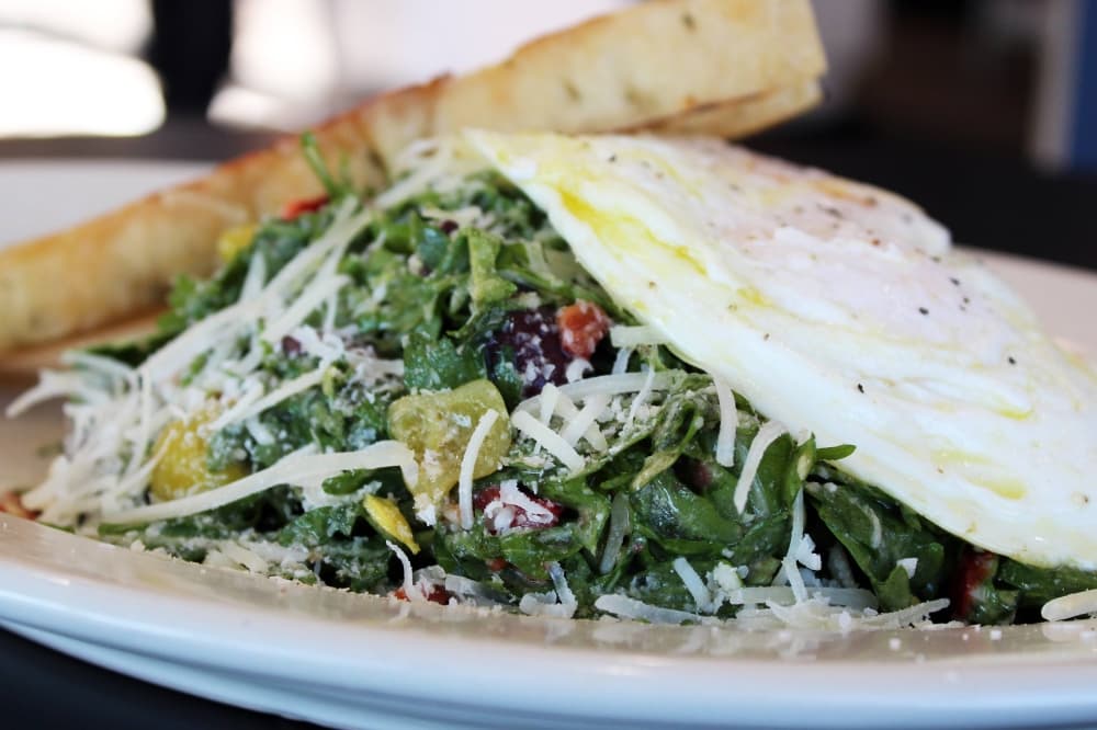 Salad topped with two over-medium eggs and a slice of focaccia bread. 