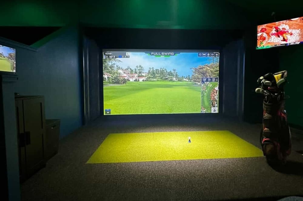 A dimly lit golf bay is shown with lights shining on the putting station and TVs mounted to the walls on either side.