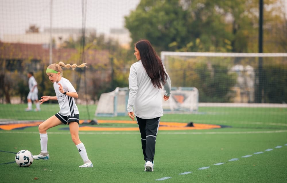 Female adult coaching a female youth on a soccer field. 