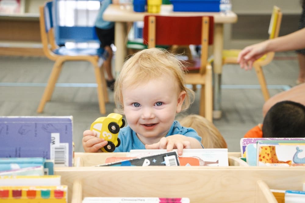 child holding a toy car near some books