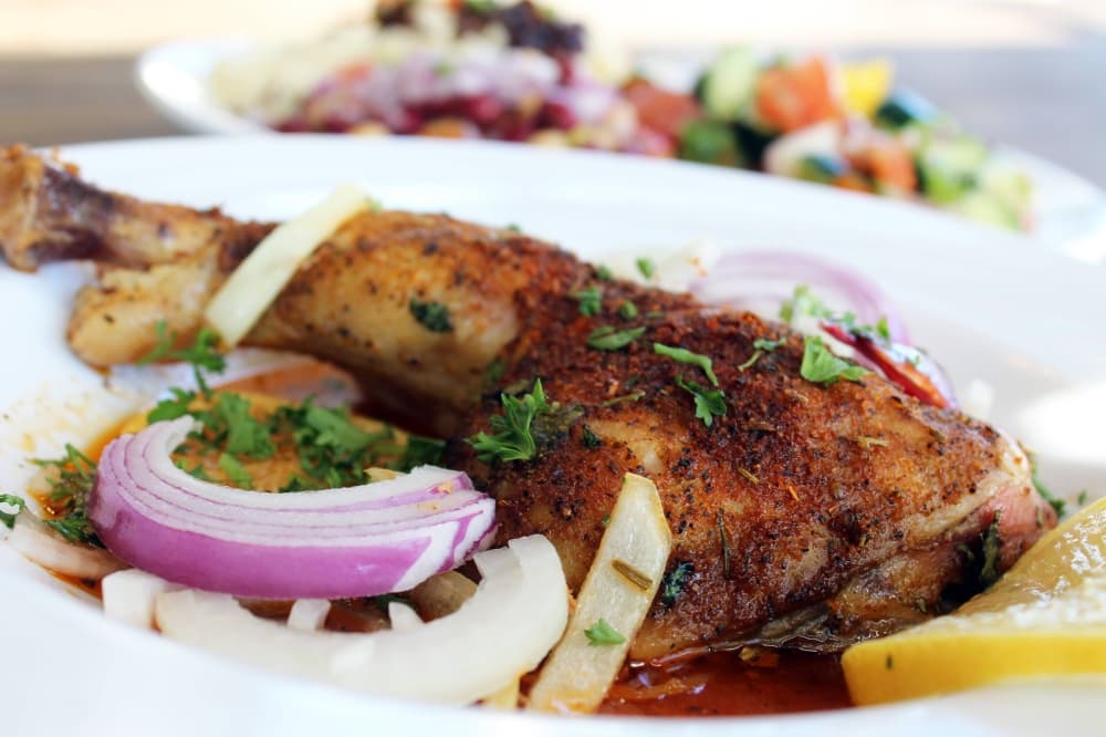 Roasted and seasoned chicken on a plate garnished with onions and lemons. 