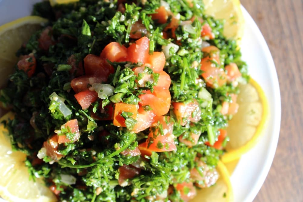 Overview of a green salad featuring tomatoes, lemon slices and seasonings. 