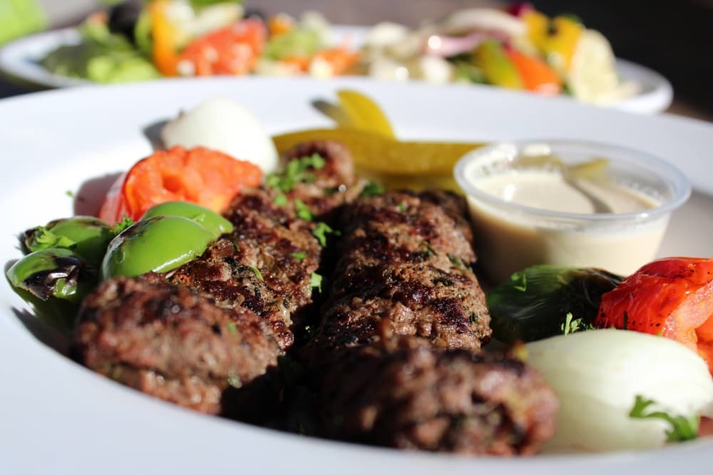 Slices of grilled beef on a plate with onion and tomato garnishes.