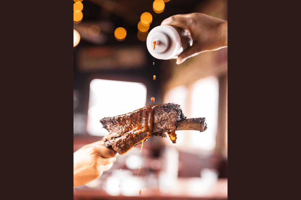 Person pouring sauce onto BBQ rib