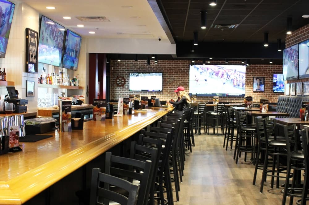 Bar with bar stools next to it and other nearby table and chair seating areas. 