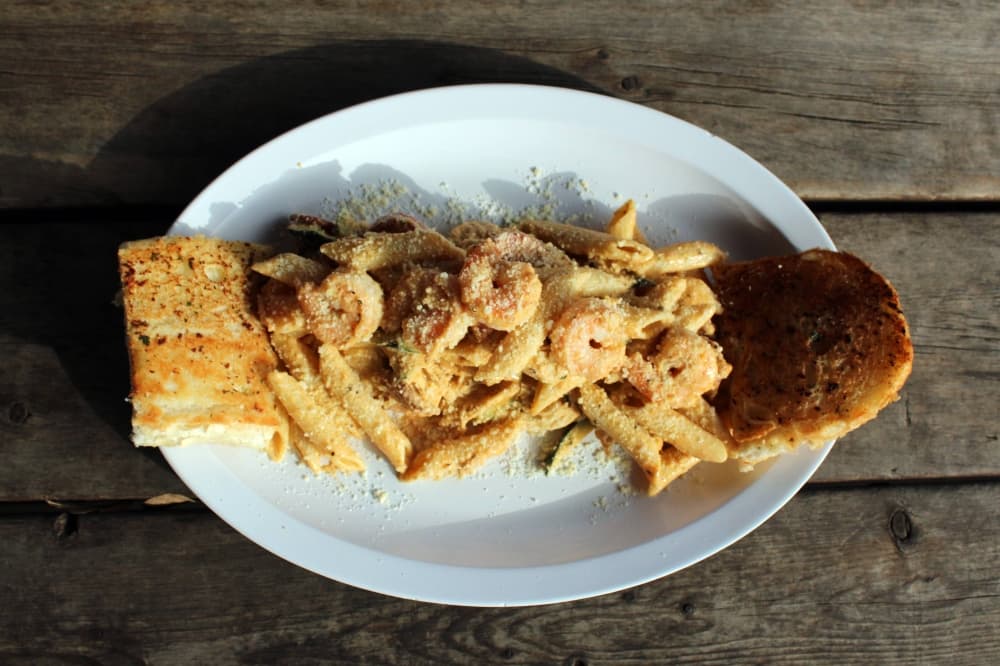 Seafood pasta flanked by pieces of bread on a white oval plate. 