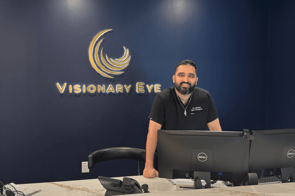 Dr. Shehz posing next to Visionary Eye sign at front desk