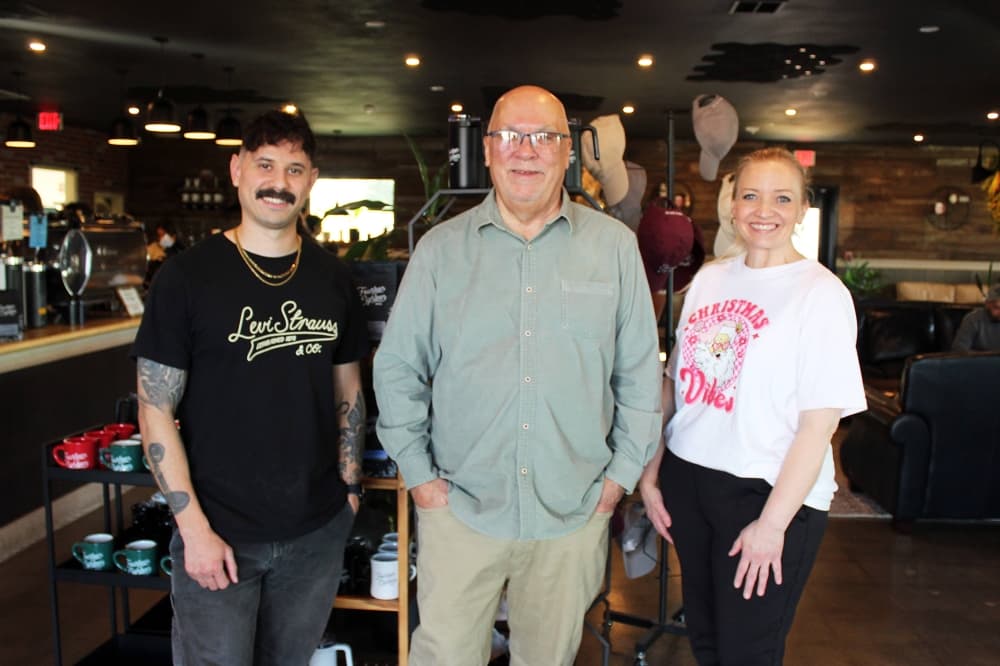 Two males and one female standing next to each other in a coffee shop. 