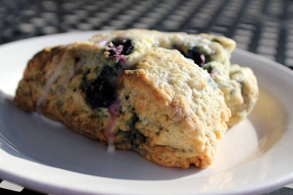 A scone featuring blueberries and light glaze on a plate. 