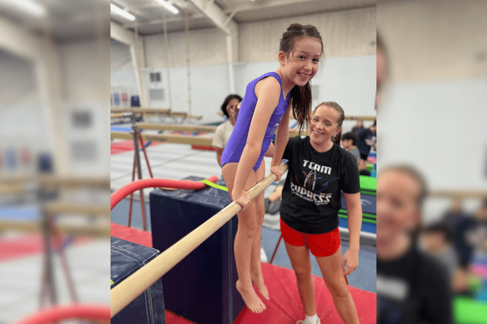 Child doing gymnastics on bar with coach next to her
