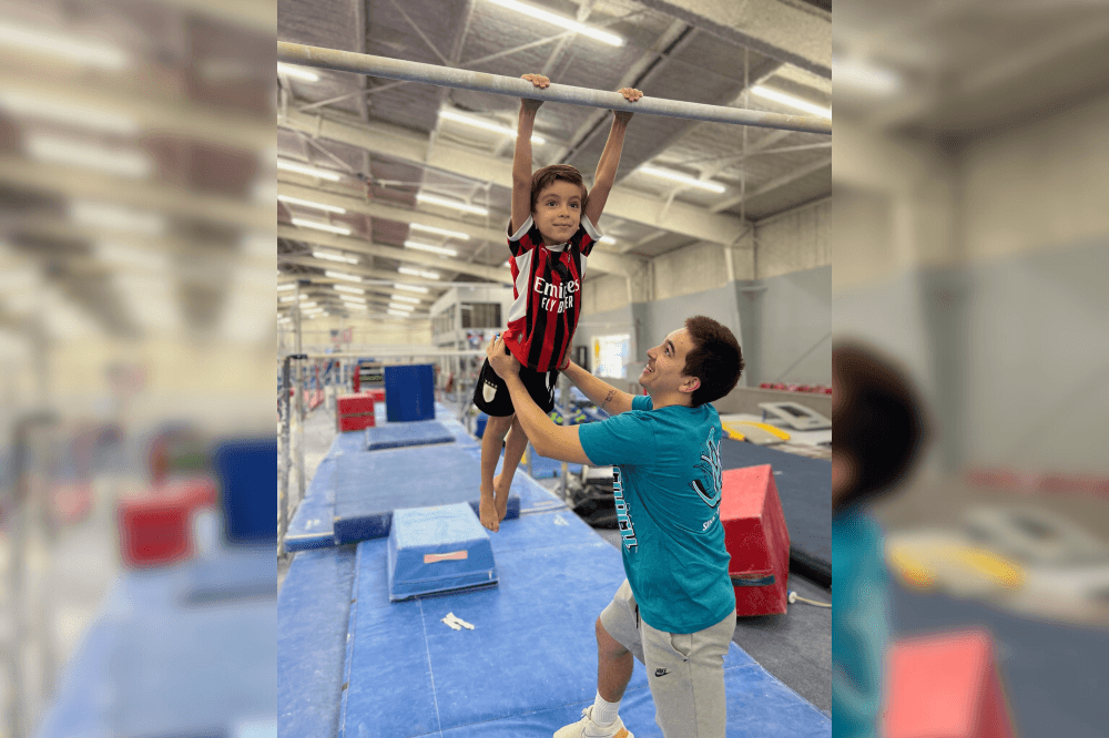 Child doing gymnastics on bar with coach next to him