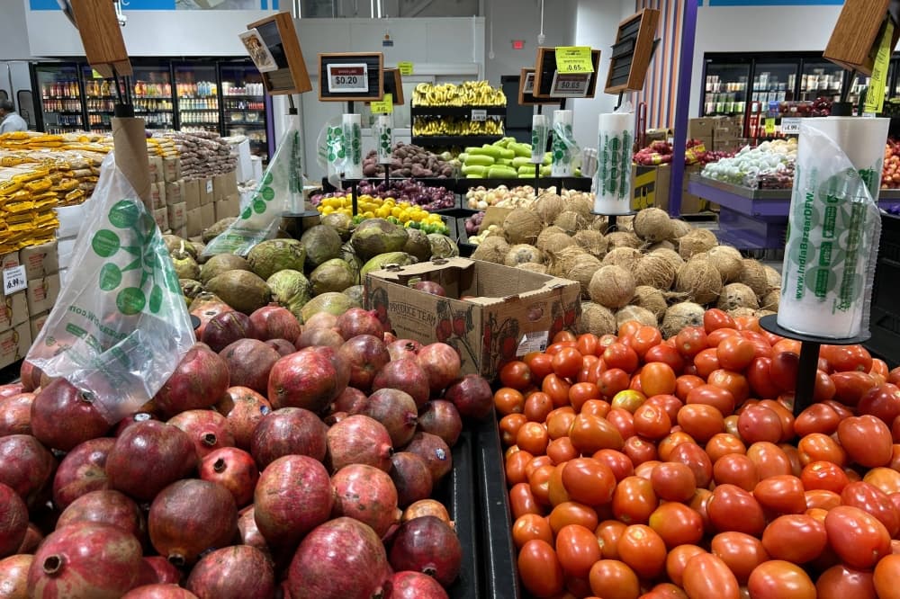 Pomegranates, tomatoes, coconuts and other fresh produce in bins in a grocery store. 