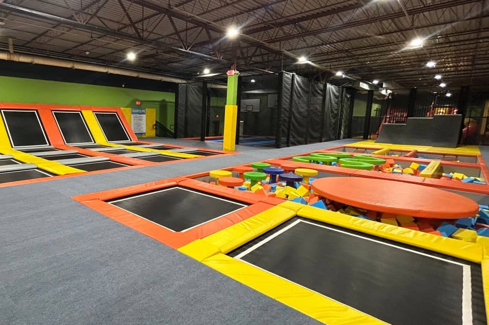 Indoor playground featuring in-ground trampolines and foam pit with balancing apparatus. 