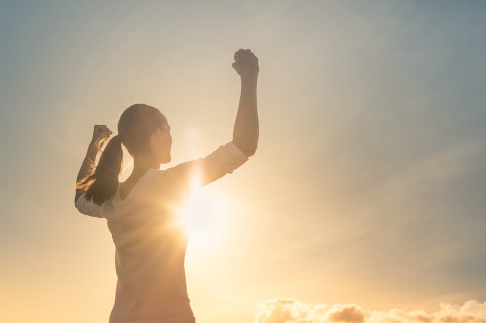 woman flexing biceps while looking towards the sun