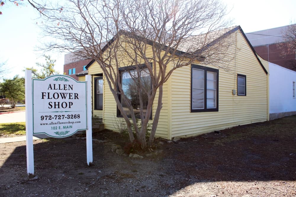 Exterior of a yellow building with a white sign in front featuring Allen Flower Shop lettering. 