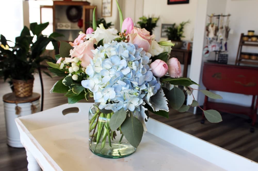 Low to the vase flower arrangement featuring hydrangea and roses. 
