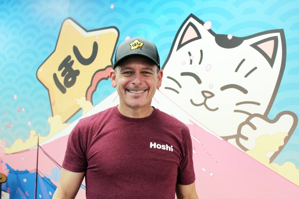 Male standing in front of a mural featuring an anime cat and a star with Japanese characters that spell 'star'. 