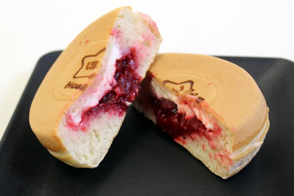 Circular baked item cut in half on a plate featuring white and pink filling. 