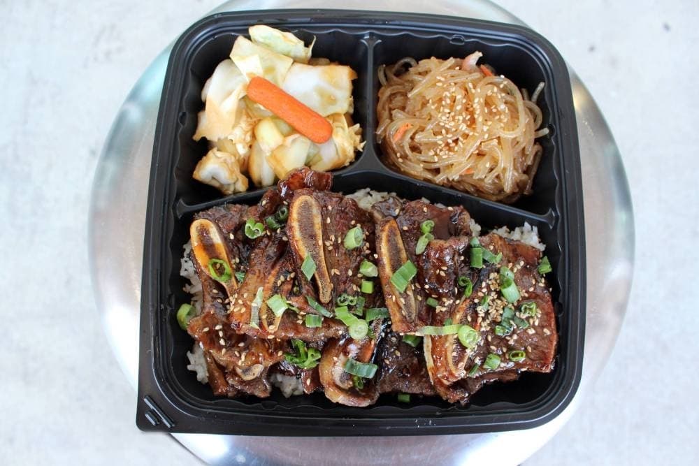 Overview of a divided dish holding a meat dish, noodles and pickled vegetables.