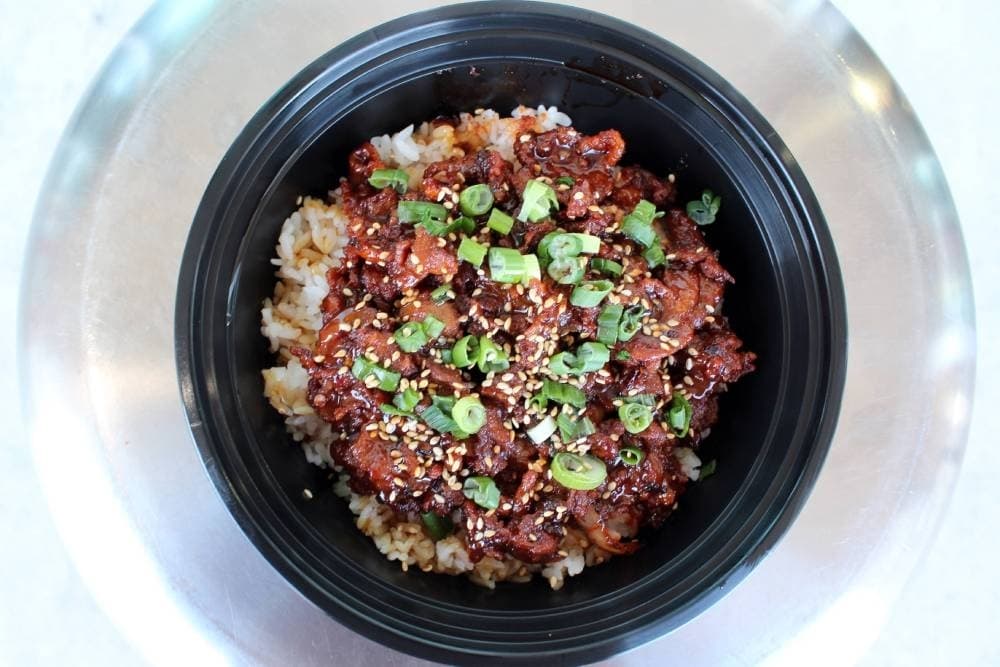 Overview of a bowl filled with a meat in sauce over rice.
