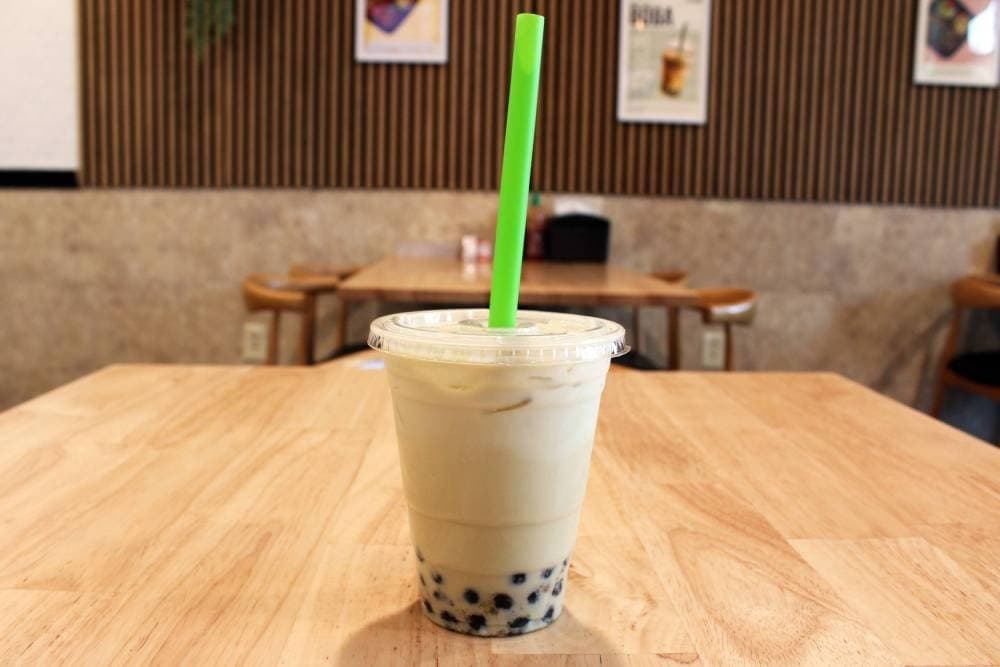 Boba tea in a plastic cup with a straw on a brown table.