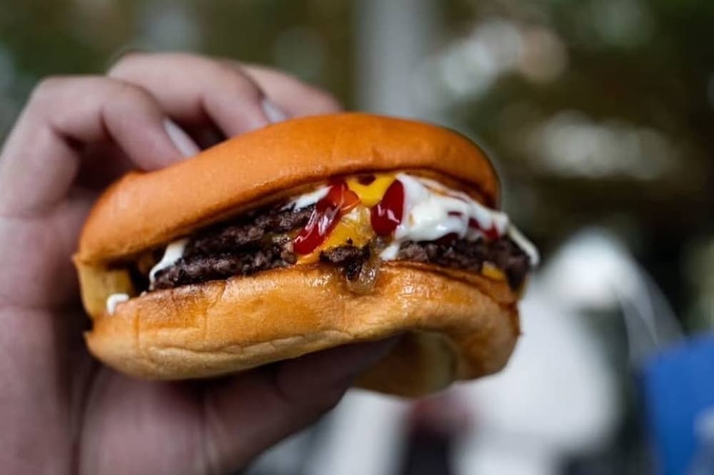 Person holding a hamburger topped with a variety of sauces on a bun.